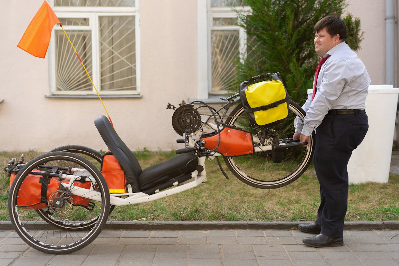 A man with Down syndrome lifts a handcycle with a yellow bag attached, standing on a street.