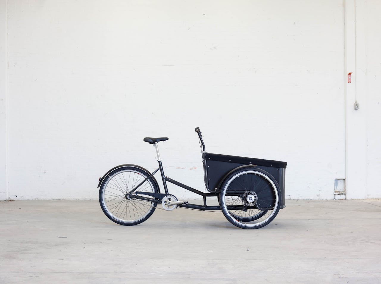 Side view of a three-wheeled cargo bike in a minimalistic indoor setting.